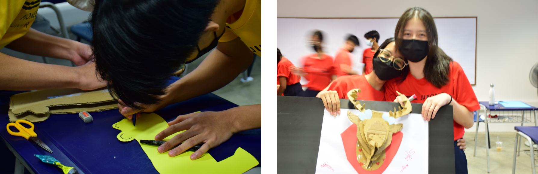 Students in yellow and red shirts work on crafts; one draws on yellow paper, two masked girls display a cardboard shield.